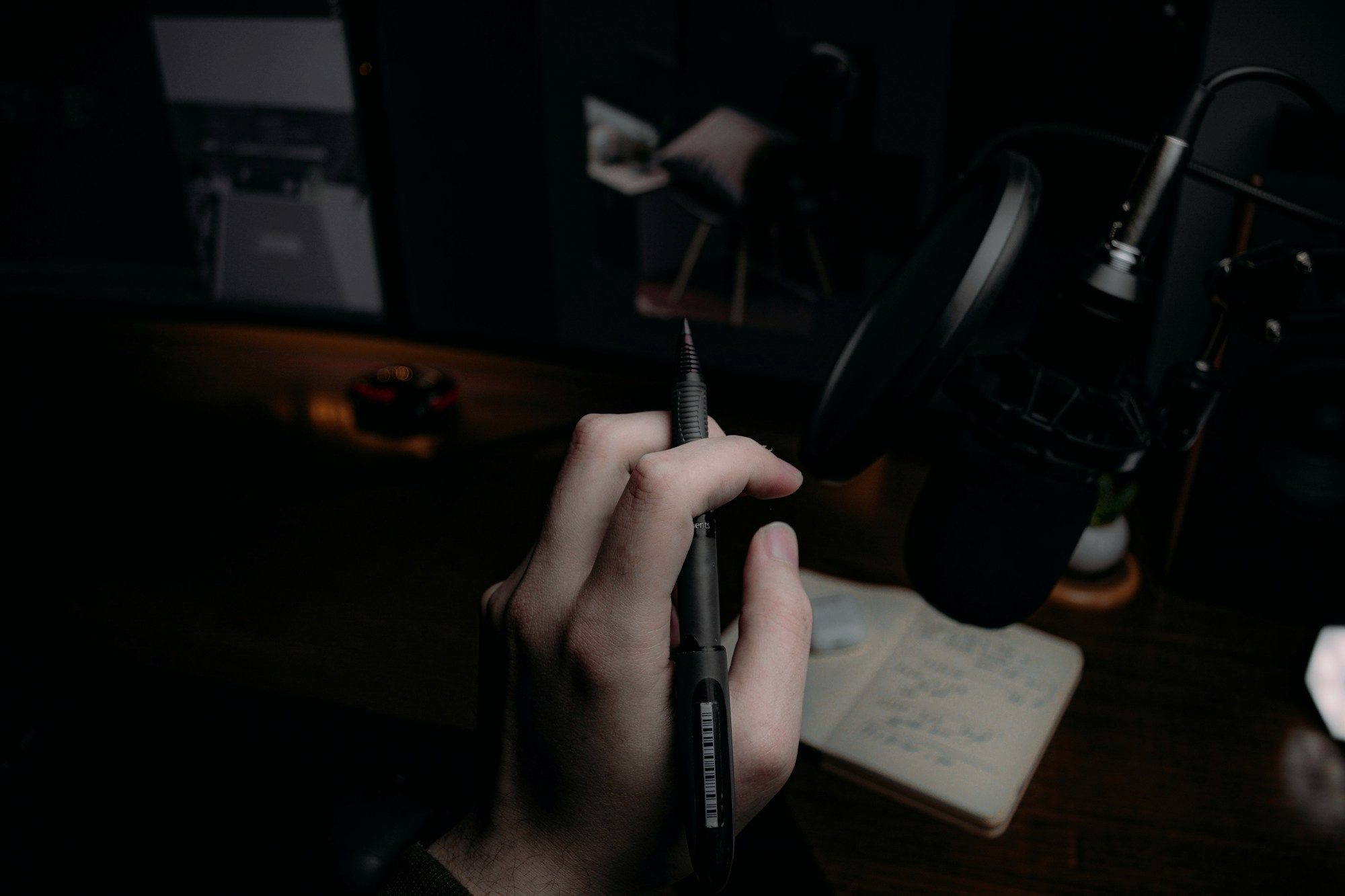 A hand holding a pen over a notebook in low light